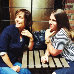 Two women sitting on a bench smiling for the camera.