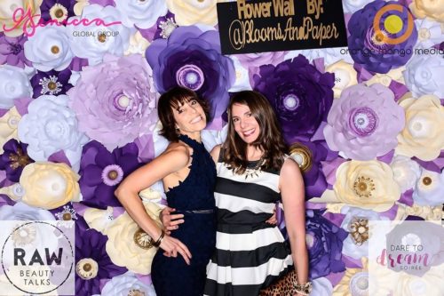 Two women posing for a photo in front of paper flowers.