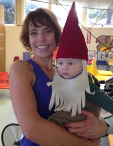 A woman holding a baby wearing a gnome hat.